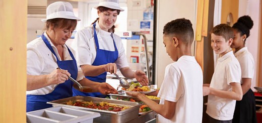 Two women serving food to a boy in a school cafeteria queue
